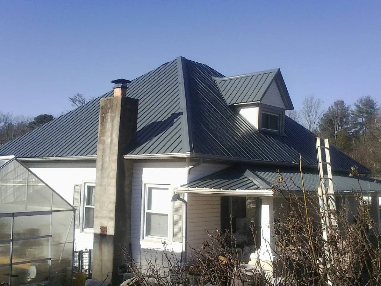Dark blue standing seam metal roof on a white farmhouse with dormer in Randolph